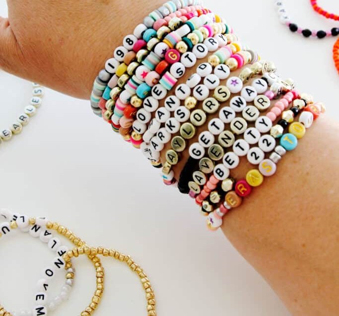 A stack of colorful beaded stretch bracelets with letter beads
